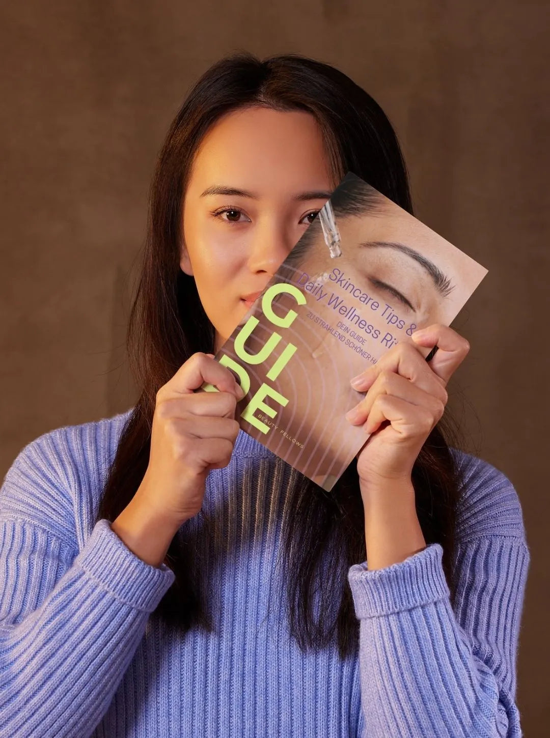 Junge Frau hält den BeautyFellows Skincare Guide vor ihr Gesicht